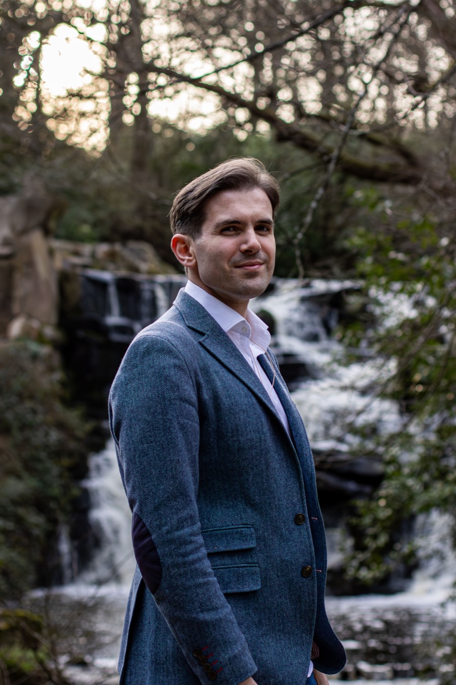 Emre Yavuz in a blue tweed jacket in front of a waterfall
